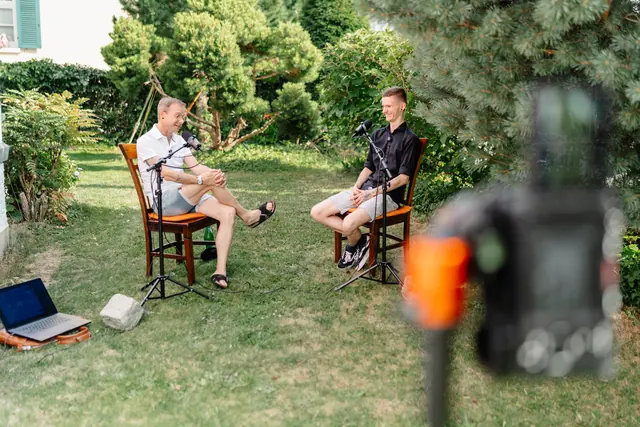Zwei Gesprächspartner bei einer Podcast-Aufnahme mit Mikrofonen und Kameras im Garten
