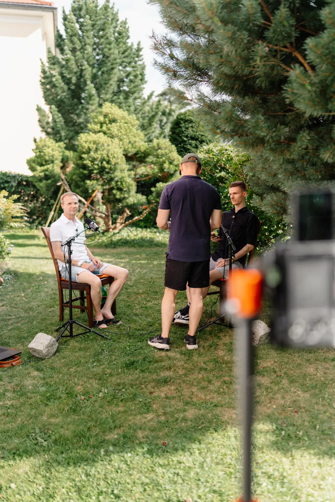 Toni stimmt eine Aufnahme mit zwei Gesprächspartnern an Mikrofonen im Garten ab