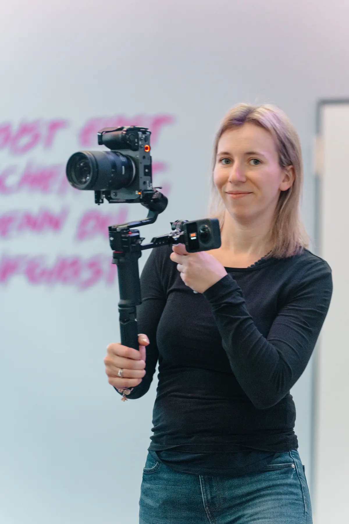 Anne hält eine Kamera auf einem Gimbal und blickt in die Kamera
