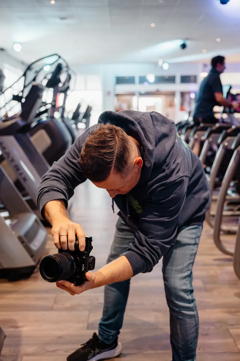 Toni filmt mit einer Kamera aus niedriger Perspektive zwischen Fitnessgeräten